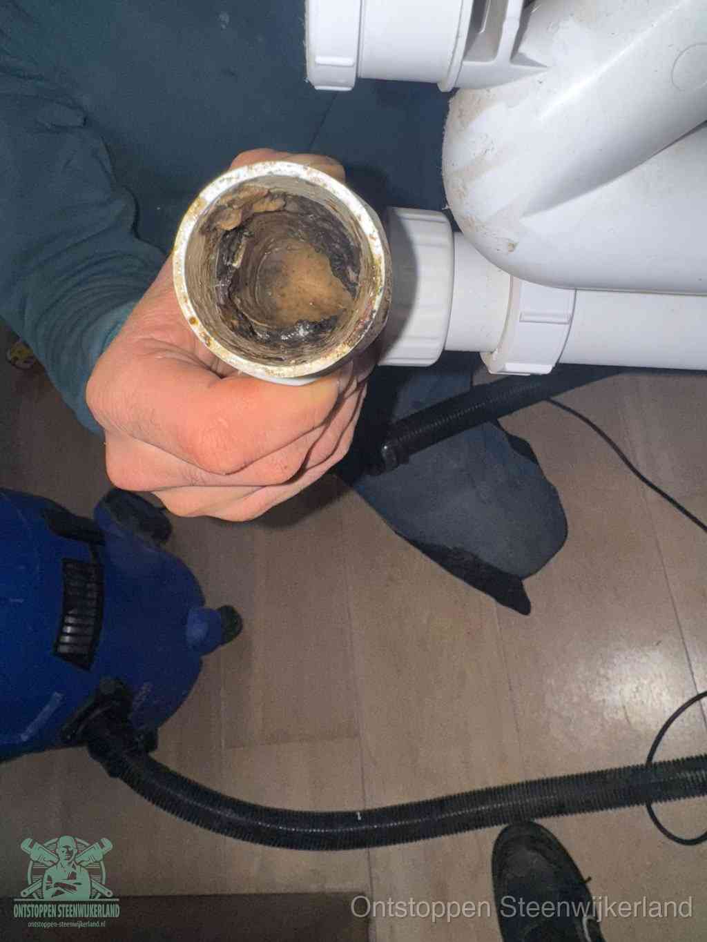 Een hand houdt een losgekoppeld PVC-afvoerbuisstuk vast dat van binnen volledig is dichtgeslibd met vet, vuil en aanslag, de meest voorkomende oorzaak van een verstopte afvoer in Steenwijkerland