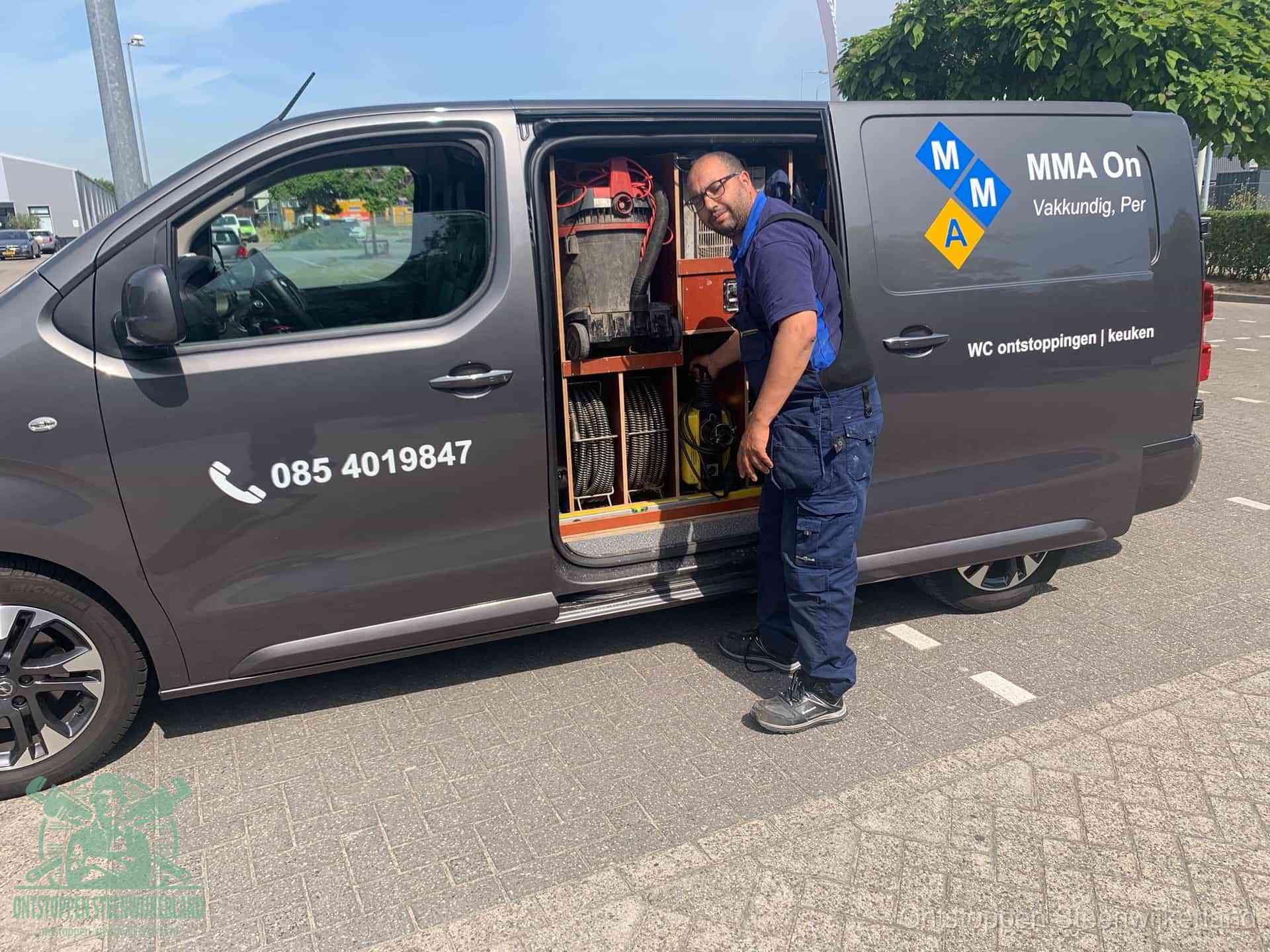 Een monteur bij de open schuifdeur van zijn bedrijfsbus op een parkeerplaats, klaar om de oorzaak van terugkerende afvoerverstoppingen aan te pakken in Steenwijkerland