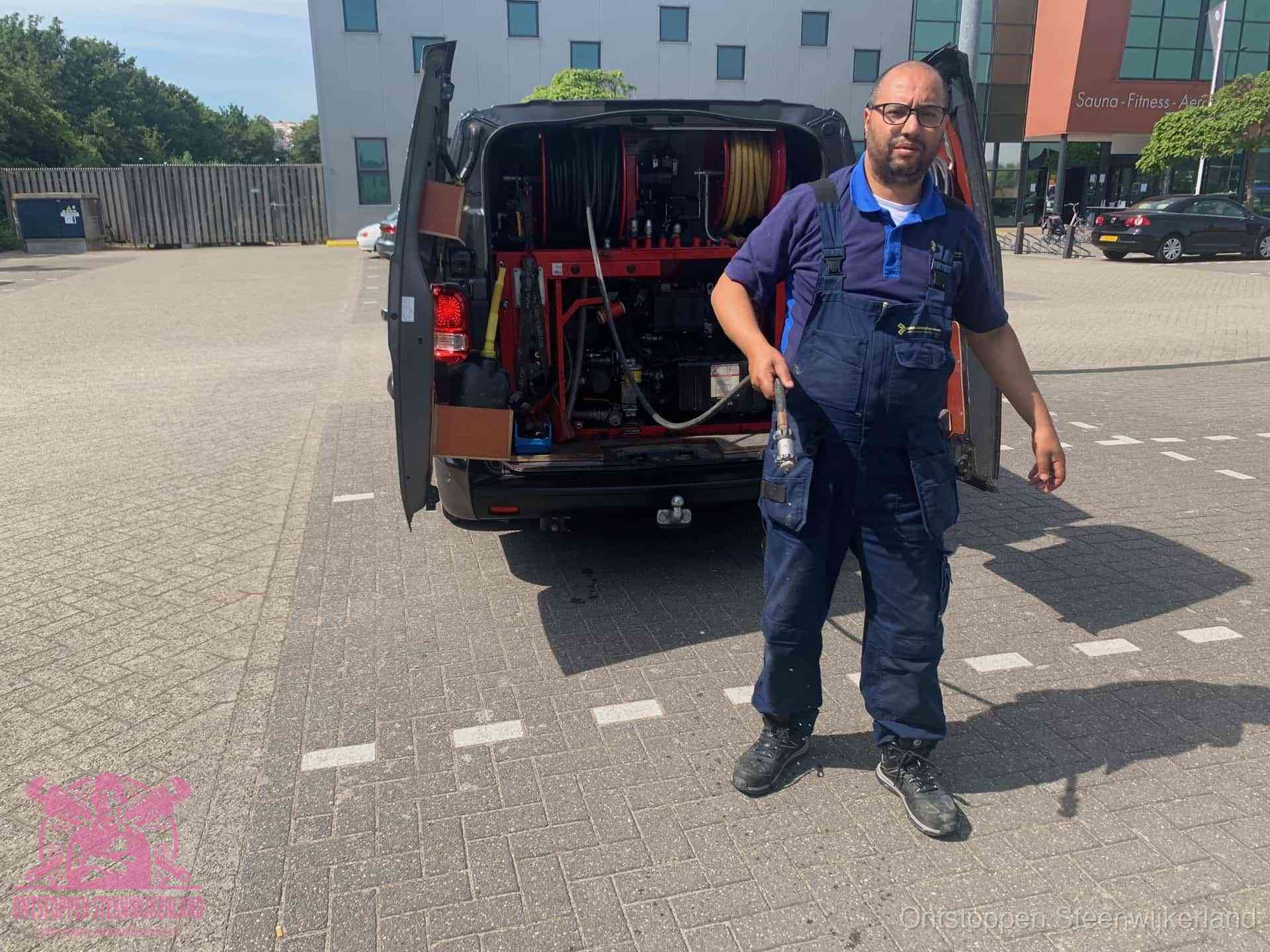 Een monteur bij zijn bestelbus met een hogedruk- en rioolreinigingsunit, klaar om de oorzaak van terugkerende wc-verstoppingen aan te pakken in Steenwijkerland