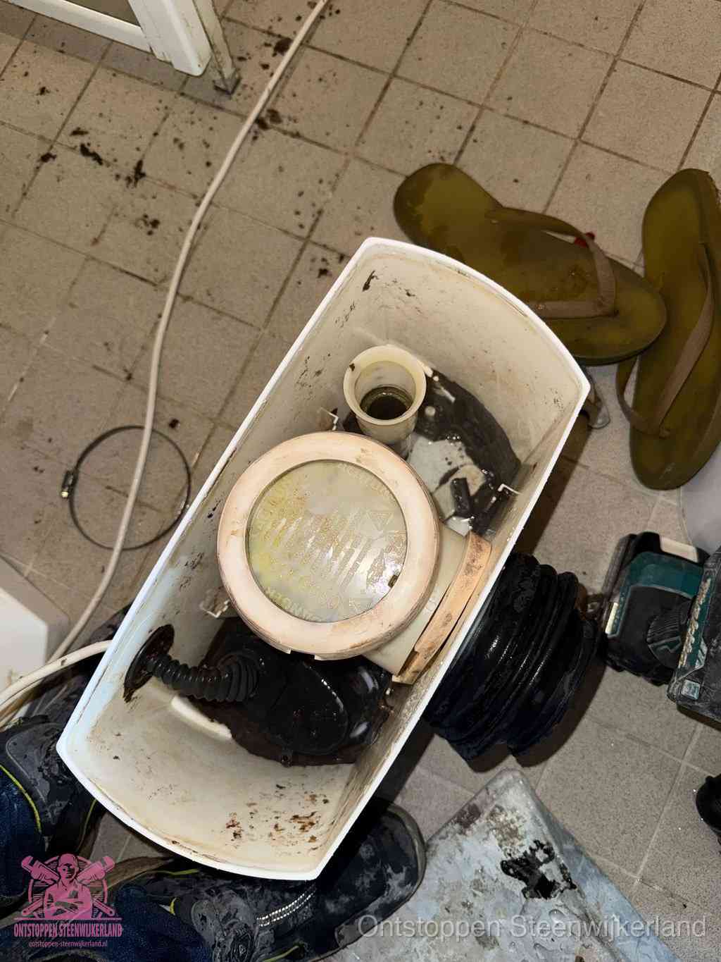 Een gedemonteerde toiletpot op de vloer met ontstoppingsveer en gereedschap ernaast, het verwijderen van een vastzittend voorwerp uit de wc in Steenwijkerland