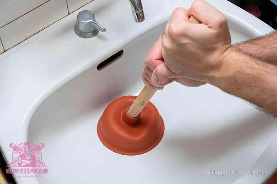 Twee handen gebruiken een rode rubberen plopper op een sanitair-afvoer om het toilet te ontstoppen in Steenwijkerland